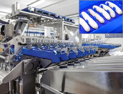 Automatisierung: Über ein Querförderband gelangen die im Pulk angedienten Nürnberger Rostbratwürste links und rechts über die beiden Verteilerrutschen auf die erste Bandstation. Füllstandsensoren überwachen die gleichmäßige Belegung. Jede Wurst ist hinsichtlich Länge, Durchmesser und Krümmung ein bisschen anders, was die automatisierte Handhabung zur Herausforderung macht