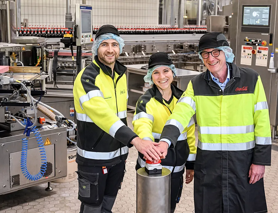 Zahlreiche Gäste wie Bürgermeister Guido Orthen (rechts) nahmen an der feierlichen Inbetriebnahme der modernisierten PET-Mehrweglinie am Coca-Cola Standort in Bad Neuenahr-Ahrweiler teil. Außerdem auf dem Bild links Hannes Bessinger (Betriebsleiter) und mittig Helen Schönknecht (Projektleiterin)