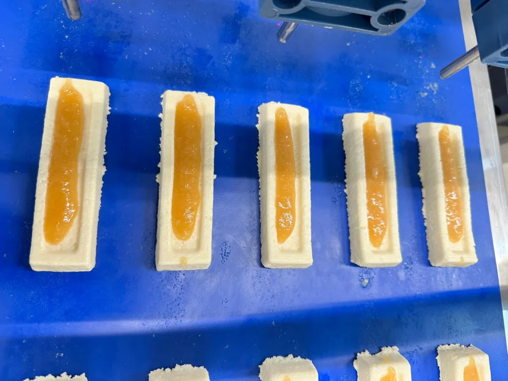 Präzise Dosiertechnik übernimmt die Befüllung der Fitnessriegel als Topping, Bild: Viscotec Dosiertechnik sorgt für die Befüllung der Fitnessriegel