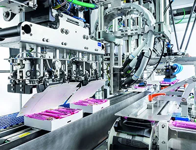 Schubert kombiniert den TLM Comfort Feeder auf der Prosweets mit einem Riegelpacker, der süße Riegel in Faltschachteln verpackt